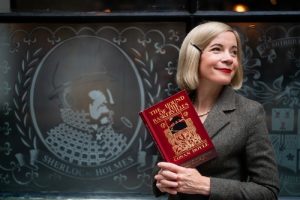 Lucy Worsley holding a copy of The Hound of the Baskervilles in front of The Sherlock Holmes Pub in London