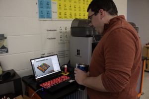 A man stands in front of a laptop looking at a 3D printing design in the computer program CAD.