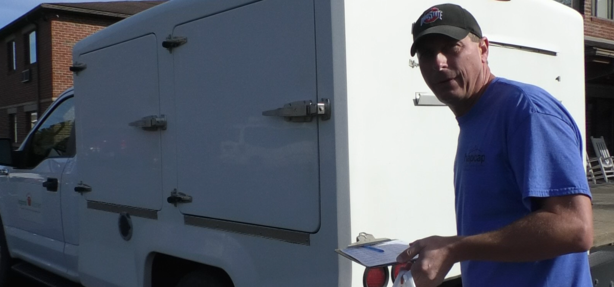 Meals on Wheels driver Josh Dean stands outside his truck with a bagged meal and clip board.