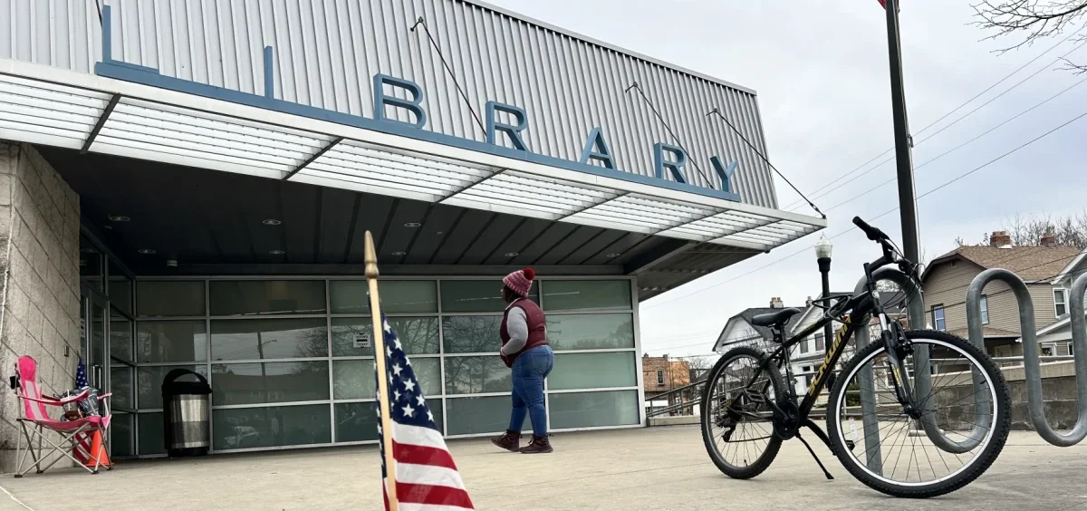 A poll worker waits for voters outside a precinct in North Columbus with an American flag in the foreground.