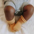 The legs of a baby who is black are on a bed sheet. The rest of the baby is attached, its just off camera.