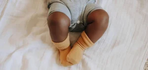 The legs of a baby who is black are on a bed sheet. The rest of the baby is attached, its just off camera.