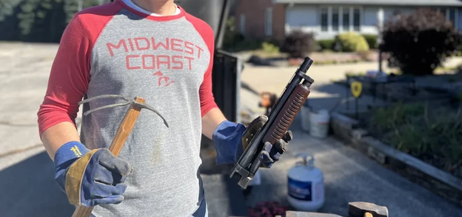 Joel Shenk wears a baseball tee and a hat as he holds parts of guns to turn into tools.