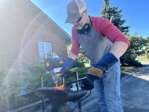 Joel Shenk smashes his mallet into a hot piece of metal on his anvil.