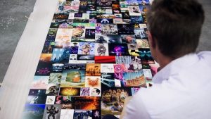 back of man's head as he looks at many, many postcard sized pieces of art on a table