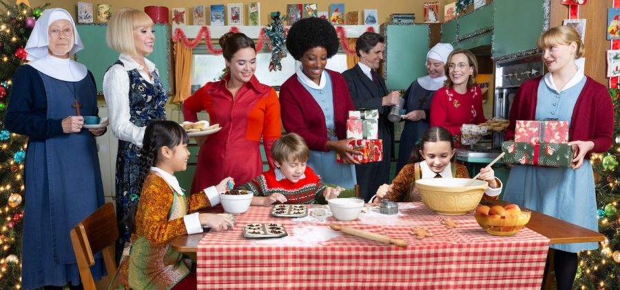 Midwives, children and nurses around a Christmas holiday table making cookies. two adults holding gifts in kitchen decorated for the holiday.