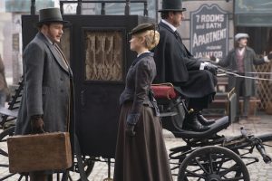 Shown L-R: Patrick Nash (Felix Scott), Eliza Scarlet (Kate Phillips) standing in front of horse drawn carriage on cobblestone street