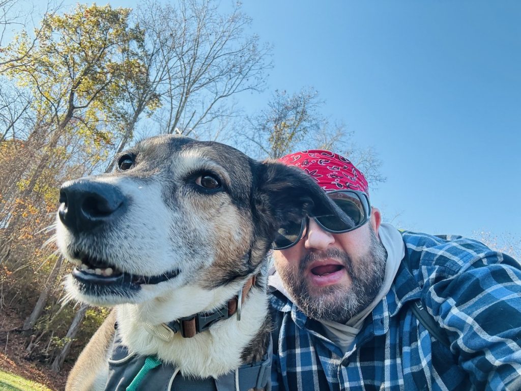 A man looks down into a camera with his dog. 