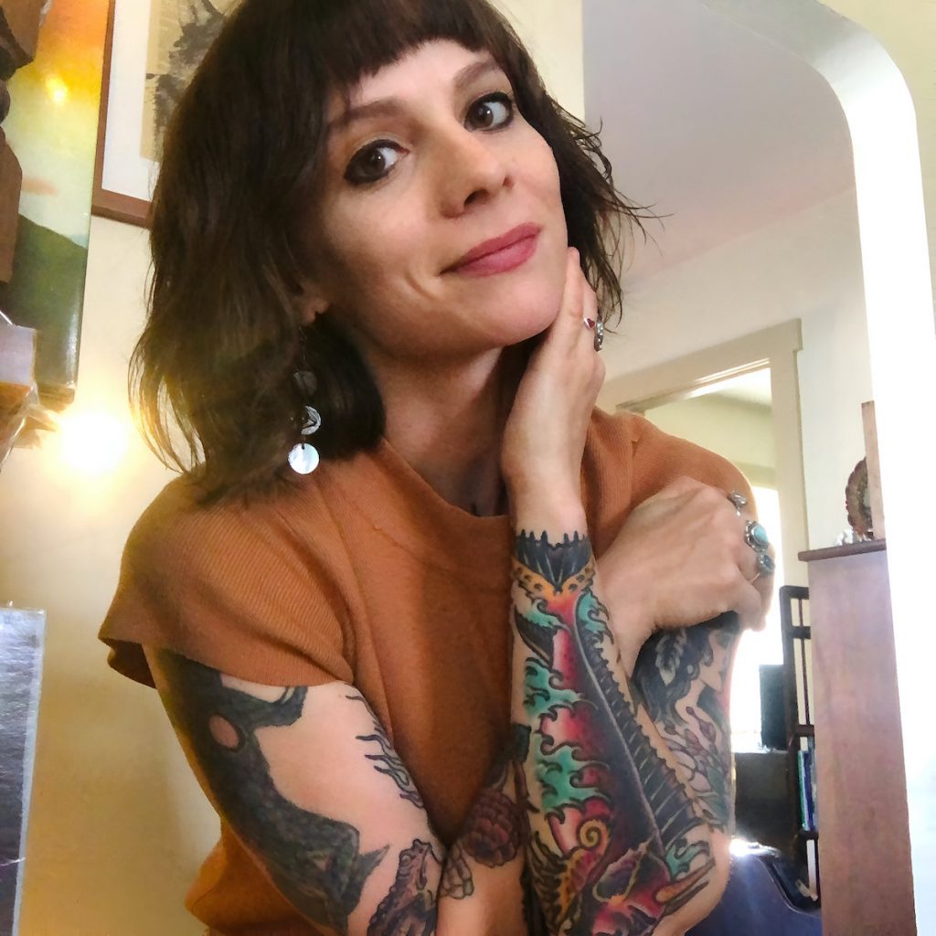 A woman with short black hair is sitting inside wearing an orange t-shirt. 