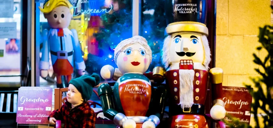 A small child sits on a bench with two giant nutcrackers