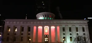 The Ohio Statehouse building at night with some sparse holiday wreaths on the side.