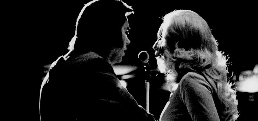 Tammy Wynette & George Jones signing a duet. Photo taken from behind them facing the audience.