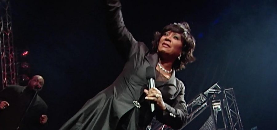 Female on stage dressed in black holding a mic and singing