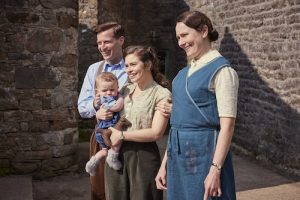 Shown from left to right: James Herriot (Nicholas Ralph), Helen Herriot (Rachel Shenton), Mrs. Hall (Anna Madeley) all standing in front of stone building smiling at something off screen