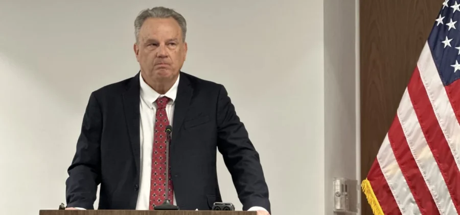 Tony Long stands with his hands on a podium at a press conference.