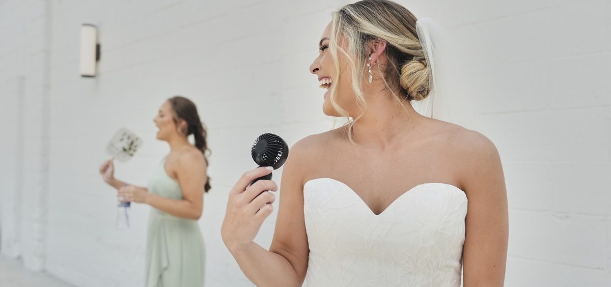 Kayla McDonald, right, uses a small electric fan to keep cool while taking bridal portraits with her sister, Jessica McDonald, left, before her wedding