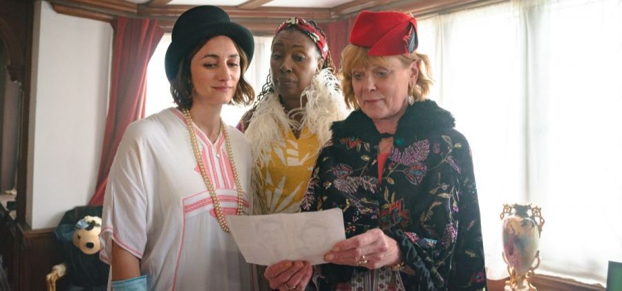 Becks, Suzie and Judith stand together looking at a photograph.