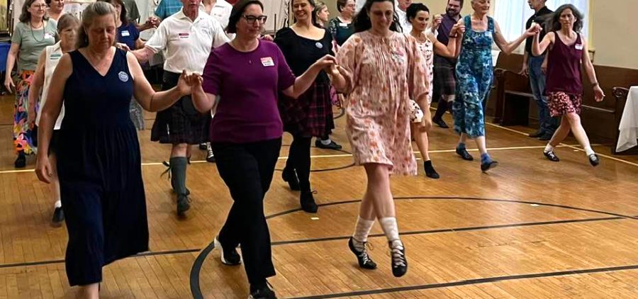 An image of people doing Scottish dance together inside.