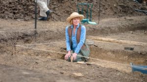 Judith Potts sits on the ground at an excavation site.