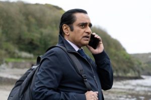 DI Sunny Khan stands outside, waring a backpack, talking on a cell phone.