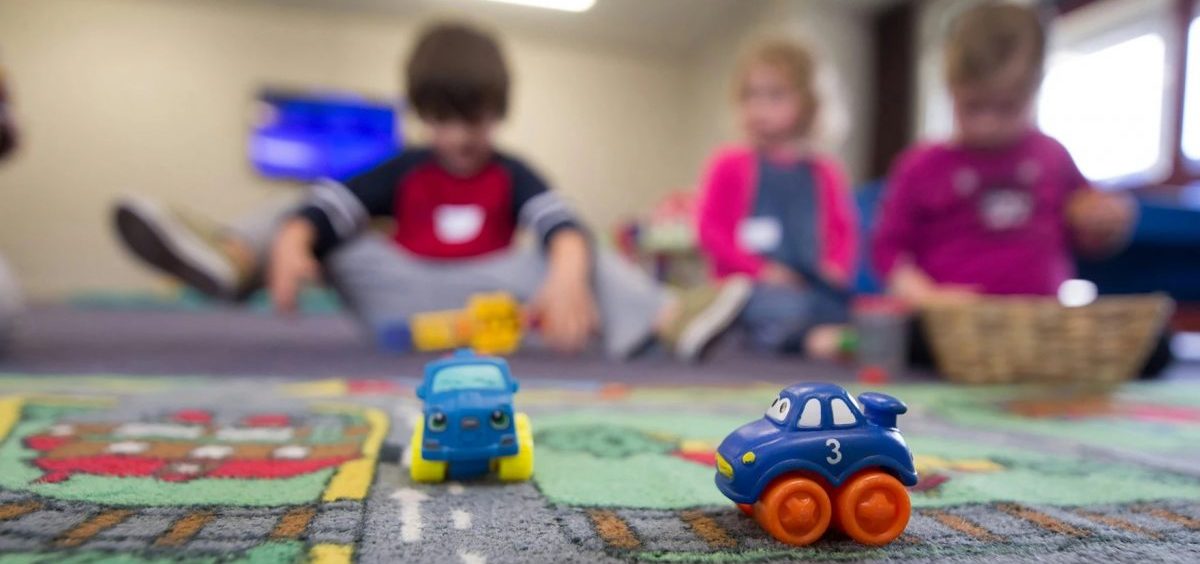 Children play on a rug designed like a city layout with two plastic toy cars with faces on them.