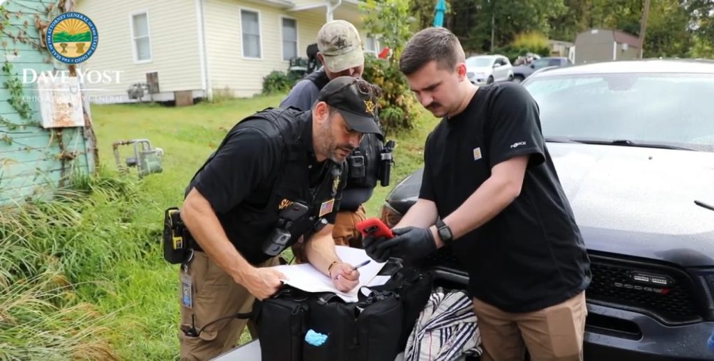 A screenshot of a video about Operation Next Door where three law enforcement officers look at a phone.
