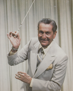 Lawrence Welk pictured in a suit holding a baton