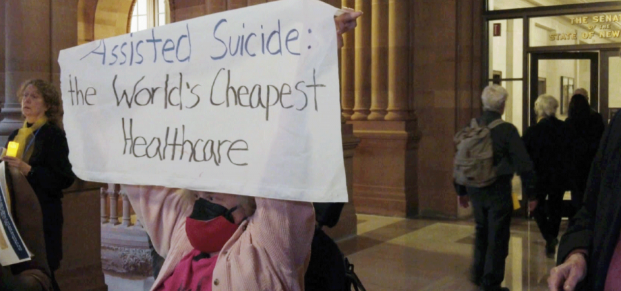 A woman holds a sign the reads "assisted suicide: the worlds cheapest healthcare"