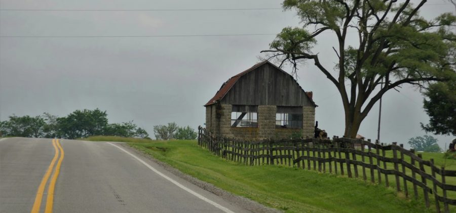 A cinder block barn sits along a wooden fence and rural road.
