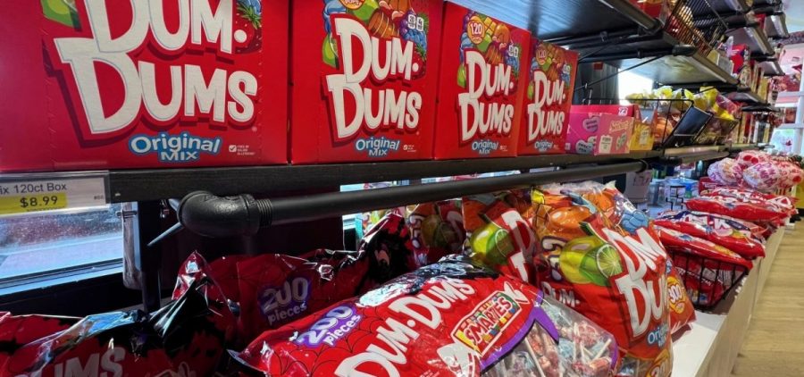 A grocery store shelf is filled with bags of Dum-Dums.
