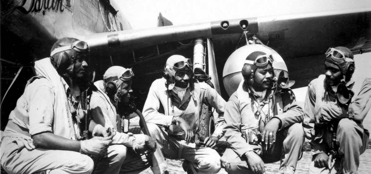 Members of the Tuskegee Airman kneel in front of a plane.