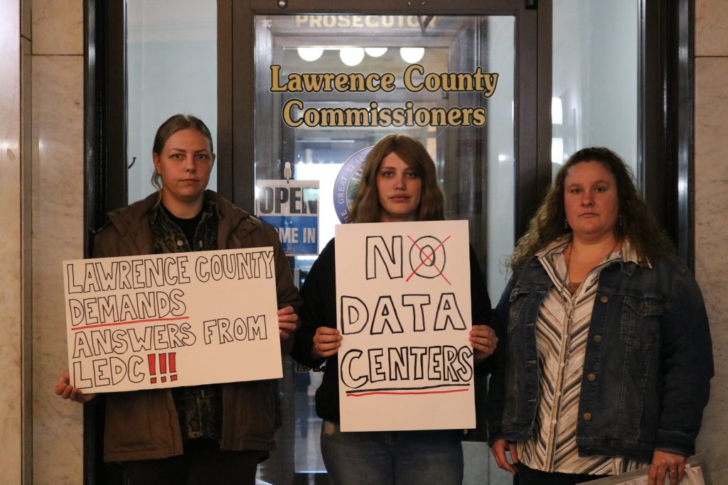 Danielle Fletcher, Katie Hill and another Lawrence County resident stand outside the county commissioners' office with signs protesting an incoming data center. 