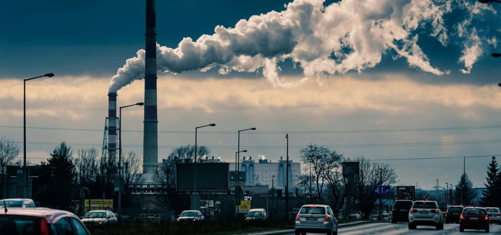 Cars drive by a power plant as a smokestack emits smoke.