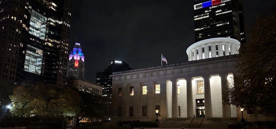 The Ohio Statehouse with the Leveque Tower and Rhode Tower behind it, both lit up in red, white and blue lighting.