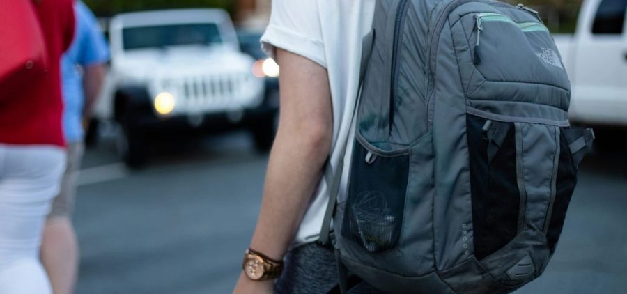 A student walks across a parking lot with a backpack on.