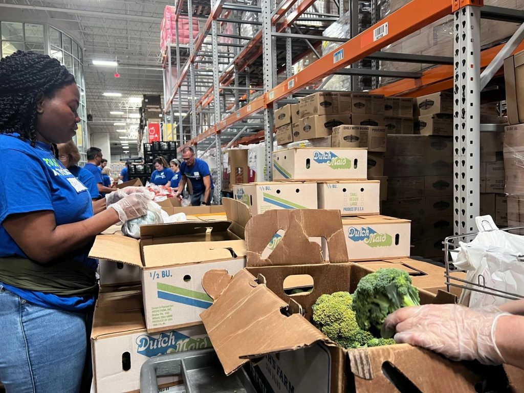 People pull out produce from cardboard boxes to later fill at a food bank.