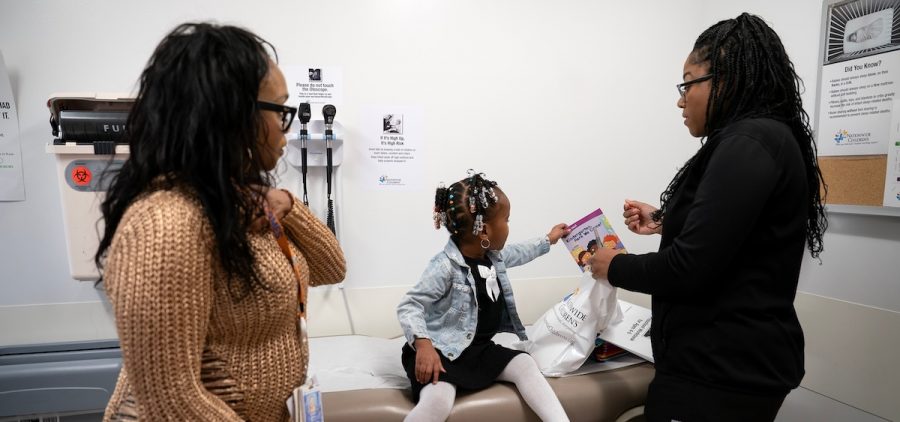Juri Sleet, 4, picks up a book from a kit given to families at Linden Primary Care Center at Nationwide Children's Hospital, while Crystal Webb, a kindergarten readiness coordinator talks with Sleet's grandmother