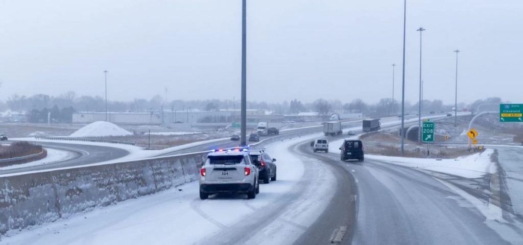 A police officer sits behind a car on the side of I-75 in Toledo after a spring snow