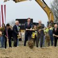 People wearing suits stand in a line and throw dirt as part of a groundbreaking ceremony.