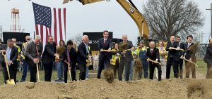 People wearing suits stand in a line and throw dirt as part of a groundbreaking ceremony.