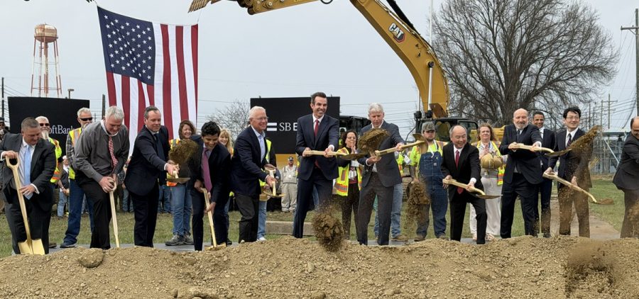 People wearing suits stand in a line and throw dirt as part of a groundbreaking ceremony.