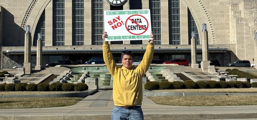 Nikki Gerber, a member of Adams County for Responsible Development, stands with a sign protesting data centers in front of a museum.