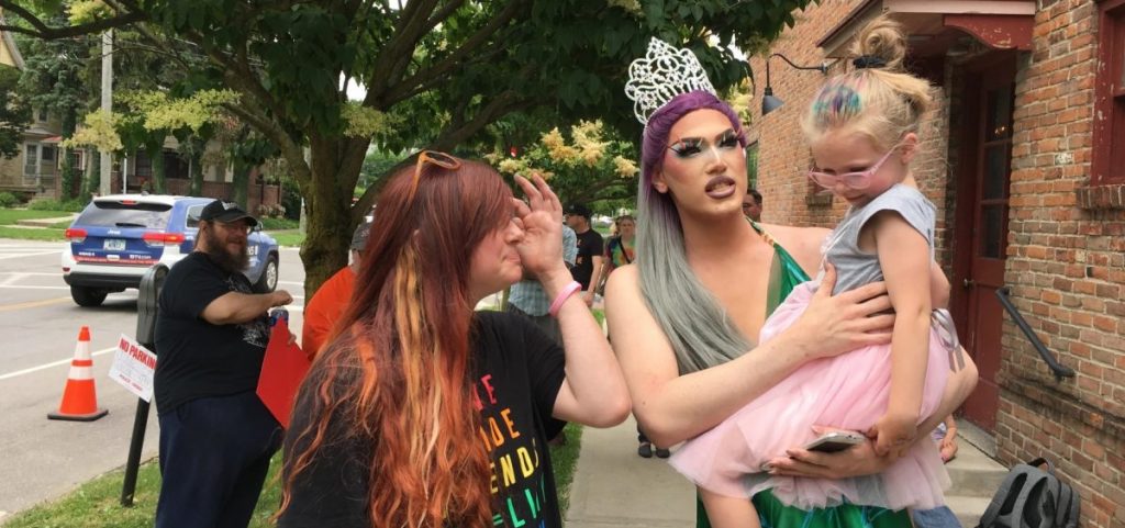A drag queen holds a child as a woman stands next to them.