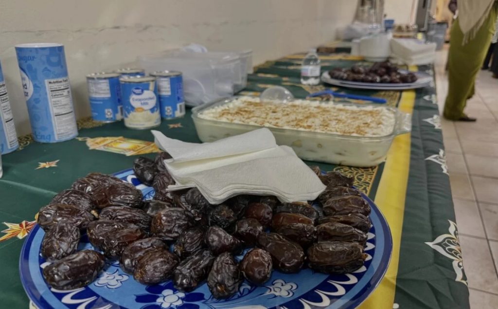 Various dishes, including a plate of dates, sit on a long table, potluck 