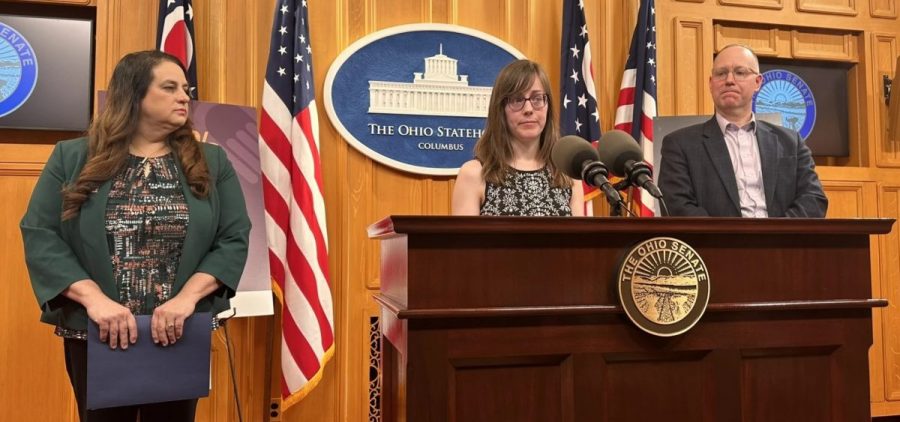 Madison Greenspan (center) shares her family's experience as she advocates for paid family leave as Sen. Beth Liston and Sen. Bill Blessing look on at a press conference on April 23, 2026.