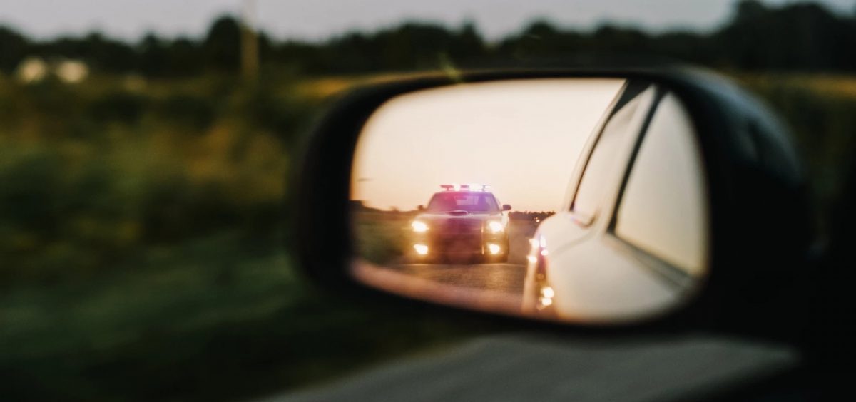 A police car has its lights on as seen in the side mirror of another car.