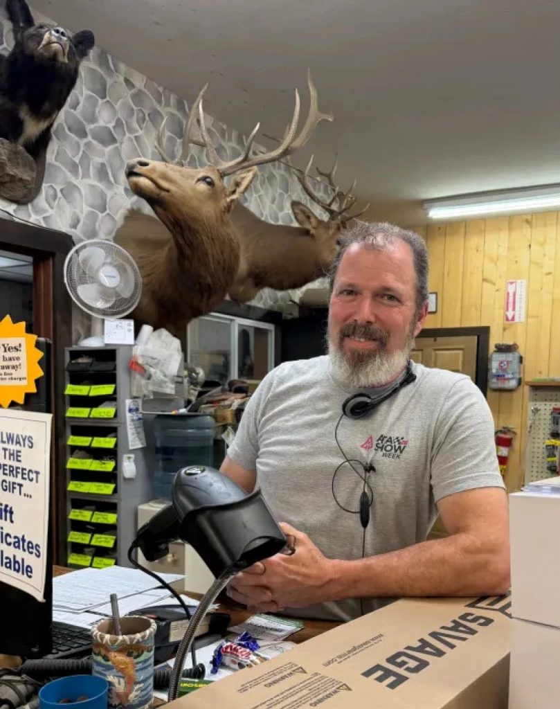 A man with a gray beard poses in a hunting supply store.