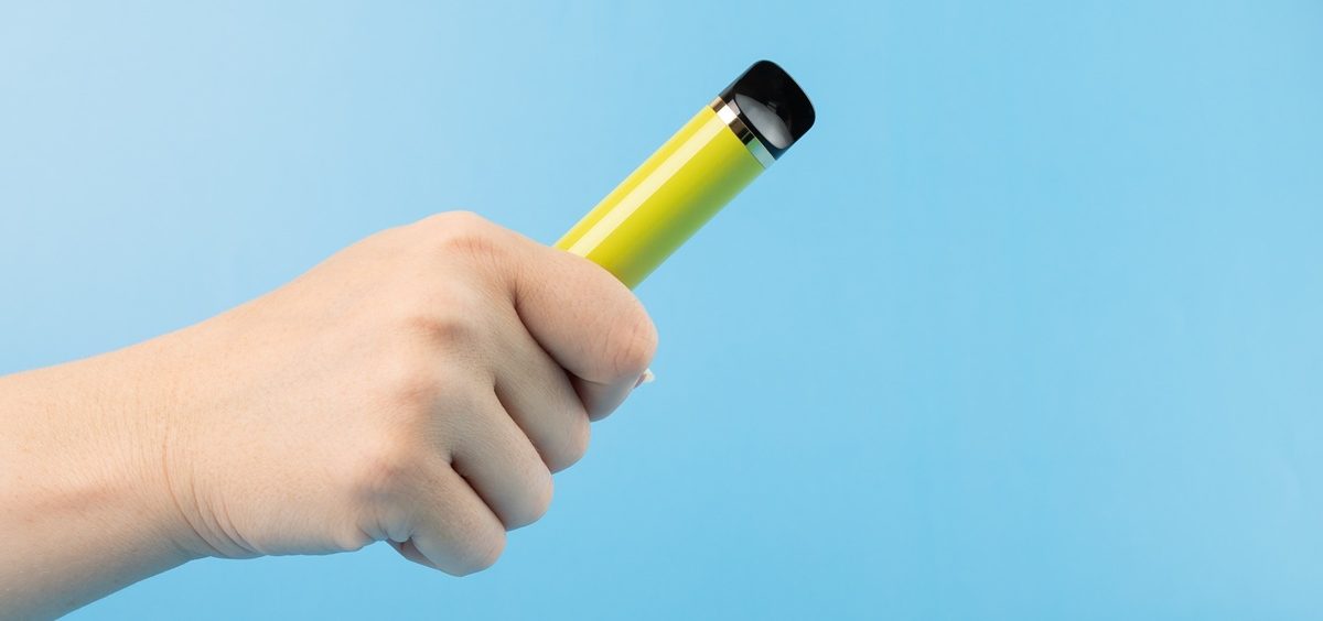disposable vape in smoker's hand on blue background