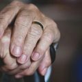 An older person's hands are crossed on top of a cane.