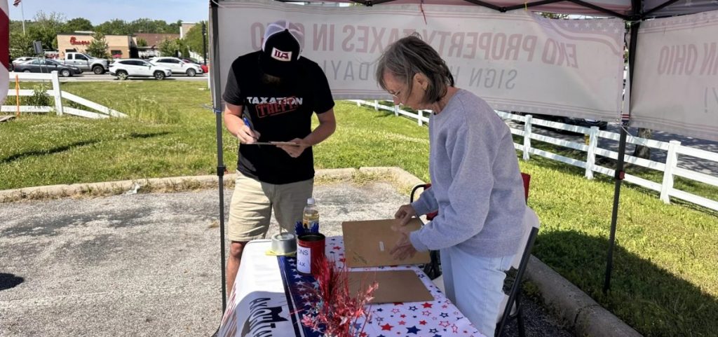 Central Ohio region captain Sue Mazzarini sorts various county petitions for the proposal to abolish property taxes in Ohio as someone stands to her right.